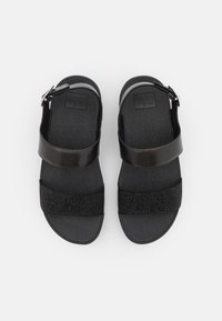 Zwarte sandalen met een soepele band, een gestructureerde voetbed en een decoratieve band met rhinestones. Verstelbare gesp sluiting bij de enkel.