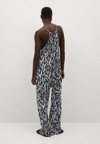 Sleeveless jumpsuit in navy blue with white pattern, made of lightweight fabric. Loose fit with wide legs and an open back design.