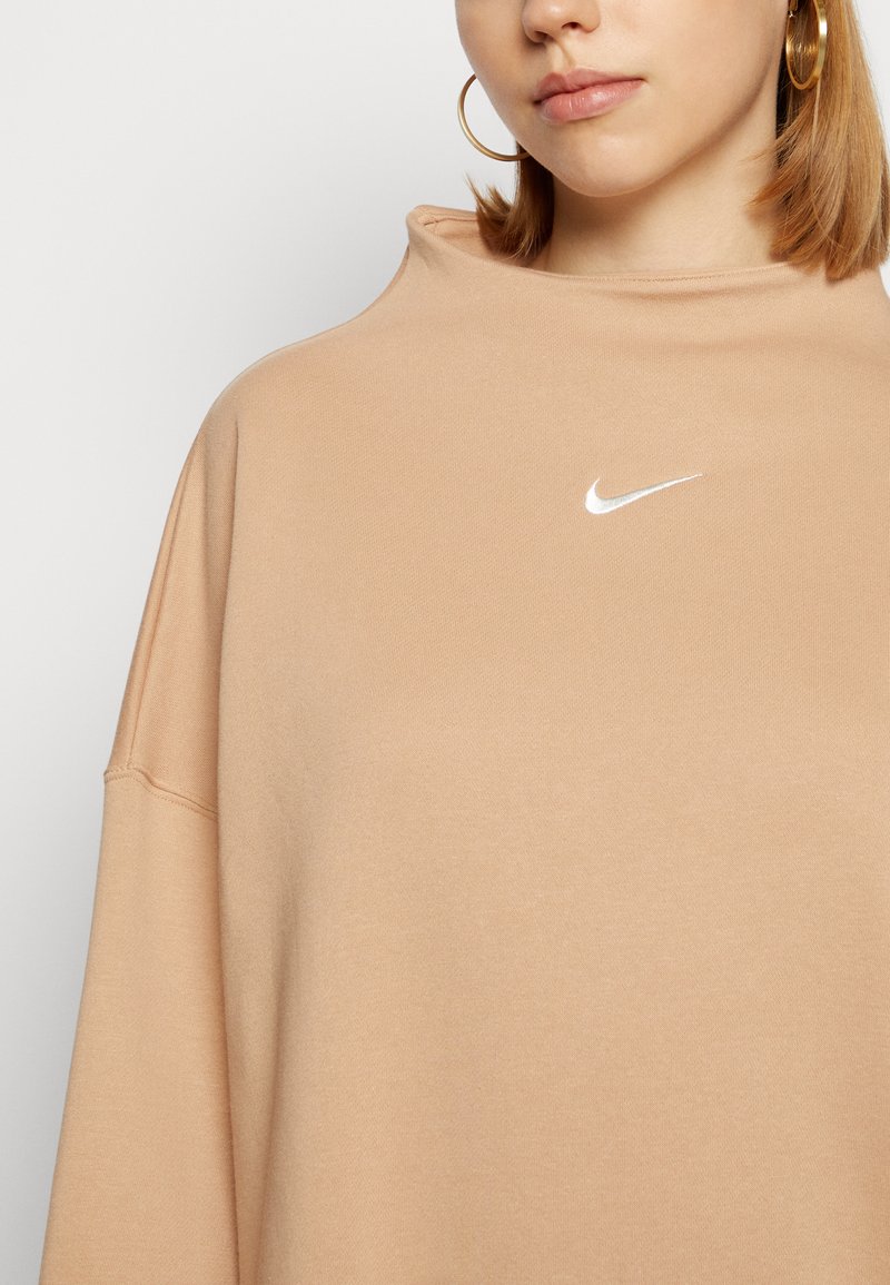 Felpa oversize beige con un collo alto e un piccolo logo Nike bianco sul petto, realizzata in un tessuto morbido e testurizzato.