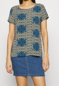 Short-sleeve top with a patterned design in blue, brown, and cream on a light background; round neckline and loose fit. Paired with a denim skirt.