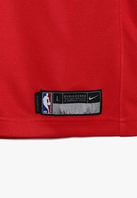 Czerwona koszulka do koszykówki z metką z tkaniny, na której widoczne są loga NBA i Nike, rozmiar L, oraz srebrny akcent z napisem "Zaprojektowane zgodnie z dokładnymi specyfikacjami."