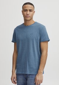 T-skjorte med korte ermer i blått, laget av et mykt og lett stoff, med rund hals og rullede ermer. Har en subtil brodert design på brystet.