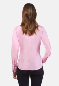 Camicia a maniche lunghe rosa con design aderente, texture liscia e polsini con bottoni. Presenta una patta con bottoni nascosta e orlo curvo.