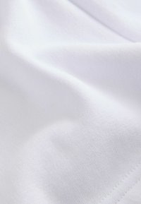 Tissu en coton blanc avec une texture lisse, présentant des plis subtils et une apparence douce. Couture visible près du bord.