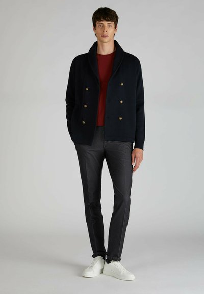 Giacca a maglia navale doppiopetto con bottoni dorati, camicia bordeaux, pantaloni grigi a scacchi e sneakers bianche. Texture liscia, vestibilità tailored.
