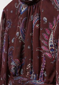 Blouse bourgogne avec motif cachemire en bleu, rose et blanc. Fabriquée en tissu doux et texturé, elle présente un col montant avec des plis.