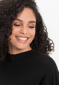 Maglione nero a coste con colletto alto, caratterizzato da una texture liscia e senza motivi visibili. La modella sorride con un trucco naturale.