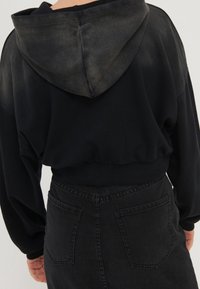 Sudadera negra recortada con una textura ligeramente desgastada y capucha adjunta, combinada con una falda de mezclilla negra de talle alto que cuenta con bolsillos traseros.