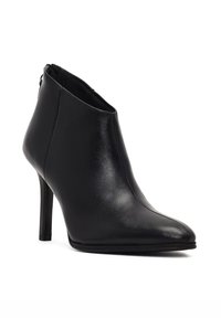 Botines de cuero negro hasta el tobillo con punta afilada, tacón alto tipo stiletto y una textura suave. Presentan un sutil detalle de costura y cierre con cremallera.