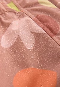 Tessuto idrorepellente di un rosa morbido con motivi circolari in arancione, verde e crema. La superficie mostra gocce d'acqua, indicando la resistenza all'umidità.