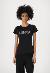 Musta puuvillainen t-paita lyhyillä hihoilla, jossa on kiiltävä "LIUJO"-logo, joka on koristeltu hopea-yksityiskohdilla rinnan kohdalla.