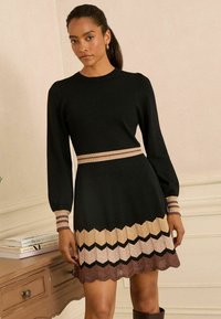 Rochie tricotată neagră cu mâneci lungi, având un tiv cu model în zigzag în nuanțe de bej, roz, negru și maro. Accentuate cu benzi în dungi la talie și la manșete.