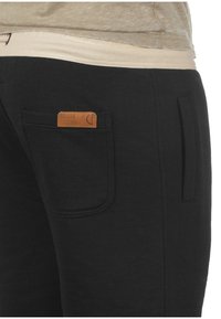 Zwarte sweatpants met een zachte textuur, voorzien van een leren label op de achterzak en een zijzak voor extra functionaliteit.