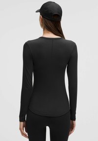 Zwarte top met lange mouwen van een stretchy, glad materiaal. Heeft een ronde zoom en een naaddetail aan de achterkant.