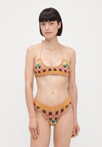Háčkovaný bikini set v prírodných farbách s mnohobarevnými štvorcovými vzormi. Top na krk a vysoké nohavičky so zúbkovanými okrajmi.