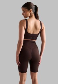 Smeđi rebrasti sportski grudnjak i biciklističke kratke hlače visokog struka, s uskim fitom, debelim trakama i suptilnim detaljem loga na pojasu.