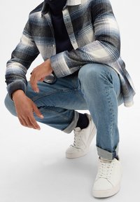 Plaid button-up shirt in navy, white, and light blue, paired with light blue jeans and white sneakers; crouched position, showing details clearly.