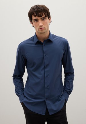 Camicia button-up a maniche lunghe di un blu scuro, realizzata in tessuto leggero e morbido; presenta un colletto a punta e un sottile dettaglio della tasca frontale.