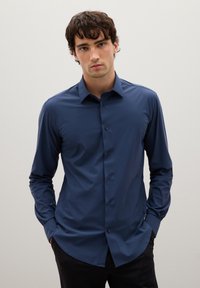 Camicia button-up a maniche lunghe di un blu scuro, realizzata in tessuto leggero e morbido; presenta un colletto a punta e un sottile dettaglio della tasca frontale.