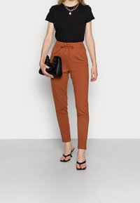 Svart t-shirt, rostfärgade åtsittande byxor med snörning i midjan och svart väska. Modellen har på sig svarta sandaletter med remmar. Slät tyg, modern skärning.