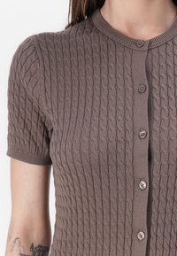 Cardigan lavorato a maglia marrone con un motivo a treccia testurizzato, maniche corte e cinque bottoni sul davanti. Tessuto morbido con una vestibilità aderente.