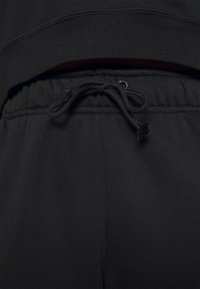 Black sweatpants feature a drawstring closure, elastic waistband, and a soft texture. The fabric appears smooth with minimal seams.