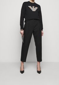 Felpa nera con emblema a strisce multicolori, abbinata a pantaloni neri a vita alta e décolleté nere a punta. Tessuto liscio e vestibilità sartoriale.