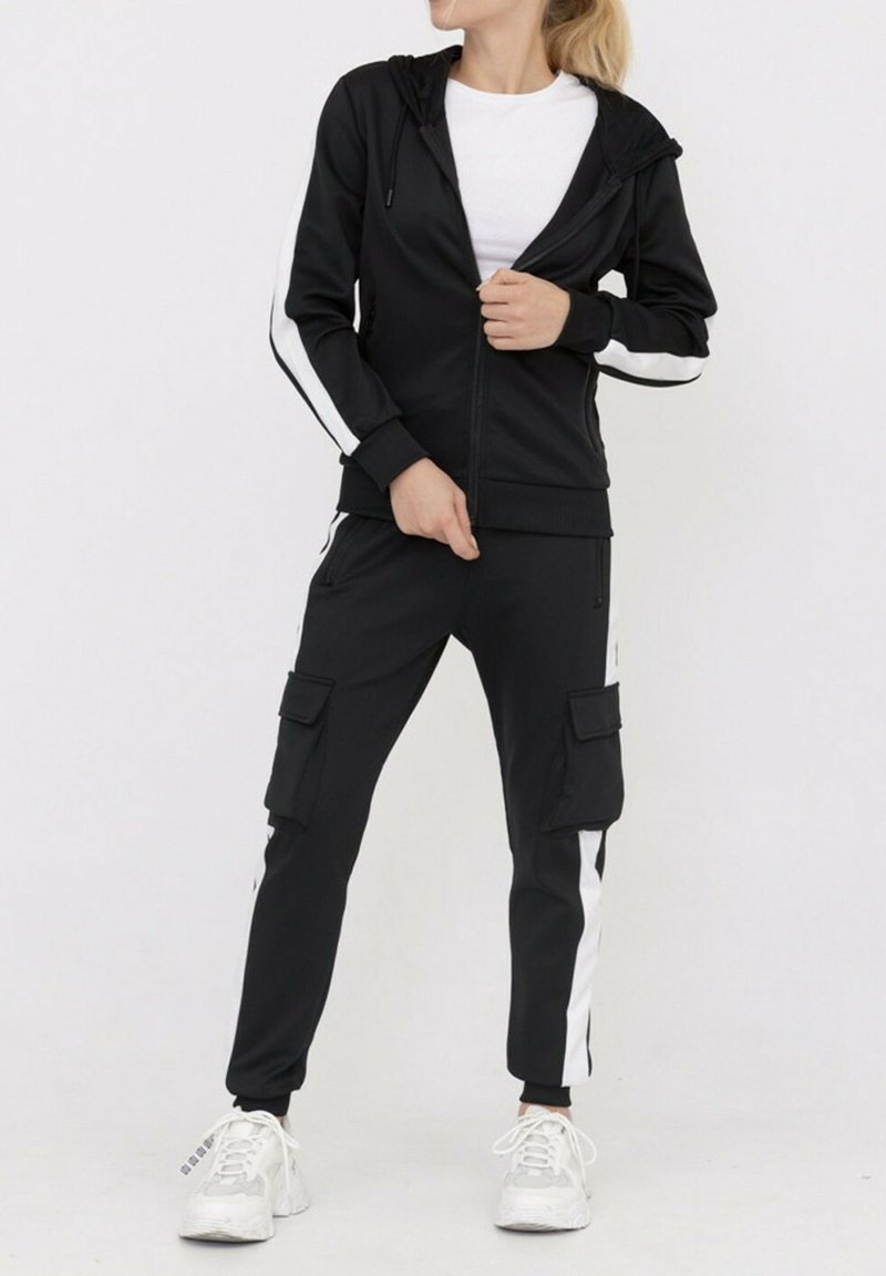 Ensemble de sport noir comprenant un hoodie zippé avec des rayures blanches sur les côtés et un pantalon cargo avec des poches latérales, fabriqué dans un tissu lisse et extensible.