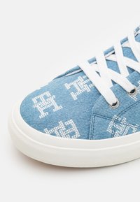 Sneaker in denim di un blu chiaro con accenti ricamati bianchi. Presenta lacci bianchi e una suola in gomma, con un design in tessuto testurizzato.