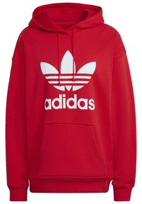Röd hoodie med en framficka, dragsko på huvan och en stor vit Adidas trefoil-logotyp över bröstet.