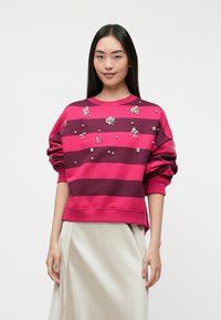 Sweatshirt listrado em fúchsia e bordeaux escuro com adornos, apresentando detalhes florais e metálicos redondos. Tecido suave com um corte descontraído.