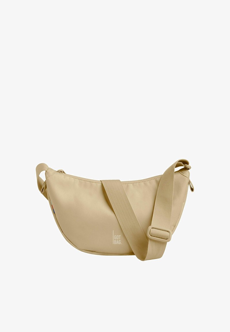 Bolso de hombro beige de tela suave, con forma curvada, correa ajustable y un logo discreto en la parte frontal.