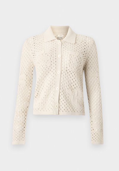 Ζακέτα από πλεκτό σε κρεμ χρώμα με μακριά μανίκια, σχέδιο ανοιχτού πλέγματος, μυτερό γιακά, κλείσιμο με κουμπιά μπροστά και δύο τσεπάκια στο στήθος με κουμπιά.