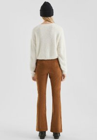 Gezellige witte fluffy trui en bruine flared corduroy broek, gecombineerd met een zwarte gebreide beanie en zwarte laarzen, gezien vanuit de achterkant.