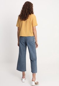 Top corto a maniche corte a righe gialle abbinato a jeans a gamba larga blu chiaro con orli sfrangiati. Scarpe bianche con tacco a blocco completano l'outfit.