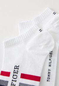 Hvide bomuldscrew-sokker med ribbede kanter, prydet med røde, blå og grå striber samt teksten "TOMMY HILFIGER" trykt på siden.
