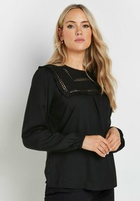 Blusa nera a maniche lunghe con colletto arricciato e cuciture decorative. Tessuto liscio con una vestibilità comoda e polsini arricciati.