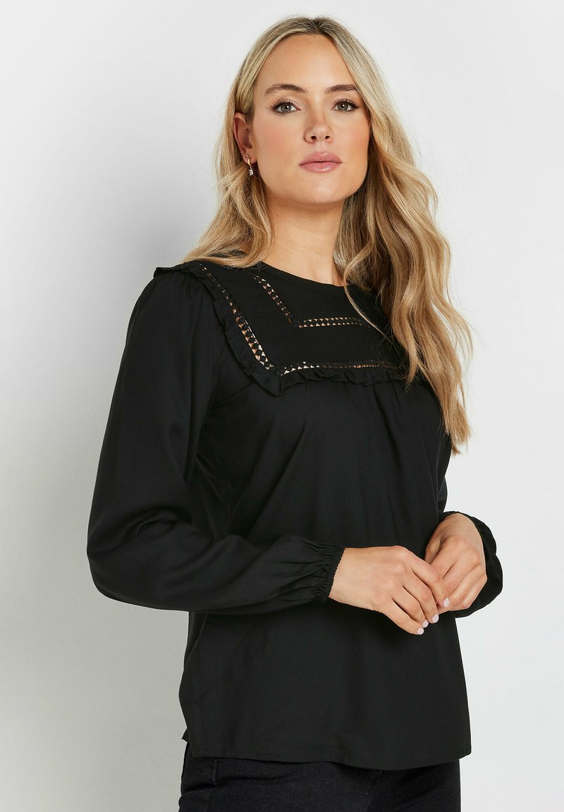 Blusa nera a maniche lunghe con colletto arricciato e cuciture decorative. Tessuto liscio con una vestibilità comoda e polsini arricciati.