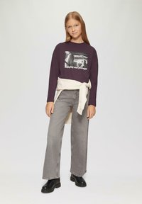 Paarse lange mouwen shirt met een grafische print, gecombineerd met lichtgrijze wijde jeans en zwarte enkellaarsjes. Effen crèmekleurige trui geknoopt in de taille.