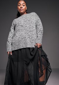 Grå stickad tröja med ett strukturerat mönster, kombinerad med en svart genomskinlig lagerkjol med spetsdetaljer och en luftig design.