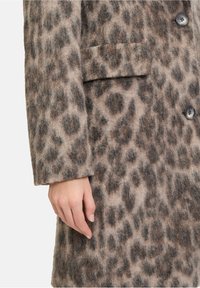 Płaszczyk w leopardzi wzór, wykonany z miękkiej, teksturowanej tkaniny. Posiada odcienie taupe i brązu, pojedynczą kieszeń na piersi oraz dwa czarne guziki.