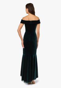 Sukně z jemného smaragdově zeleného sametu s odhalenými rameny, přiléhavým živůtkem a rozšířenou sukní. Zapínání na zip na zádech, hladká textura.