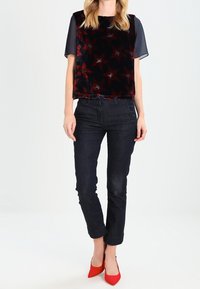 Top de terciopelo negro con estampado de estrellas rojas, mangas cortas transparentes, combinado con jeans oscuros y zapatos de tacón rojos.