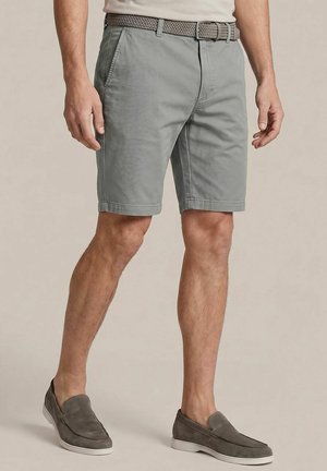 Man wearing light gray knee-length shorts with a woven gray belt and gray slip-on shoes, standing on a plain background.