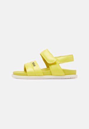 Yellow sandals with two wide straps and a back strap, made of smooth material. White sole with slight texture. Minimalist design.