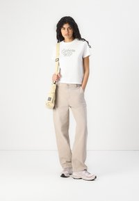 Hvit bomull T-skjorte med brodert "Carhartt WIP"-logo, beige vide bukser, lys rosa sneakers og en lys beige crossover-veske.