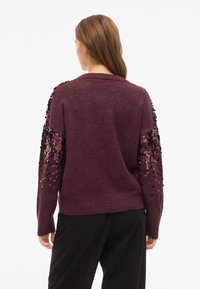 Bordni pulover z dolgimi rokavi, z črnimi in iridescentnimi bleščicami na ramenih, mehka tekstura in sproščen kroj.