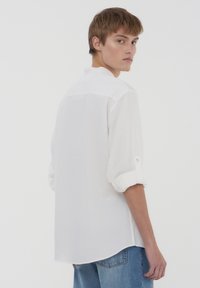 Camicia bianca a maniche lunghe con maniche arrotolate, polsini abbottonati e orlo dritto. Tessuto leggero con una finitura testurizzata, design semplice.