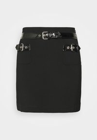 Mini-jupe noire avec ceinture noire brillante et deux lanières décoratives brillantes avec boucles au-dessus des poches avant sur fond uni.