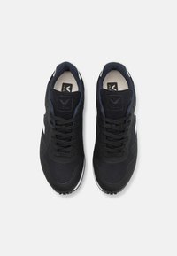 Black athletic shoes with mesh and suede upper, round toe, textured surfaces, flat laces, and a white accent. Features logo on the tongue.